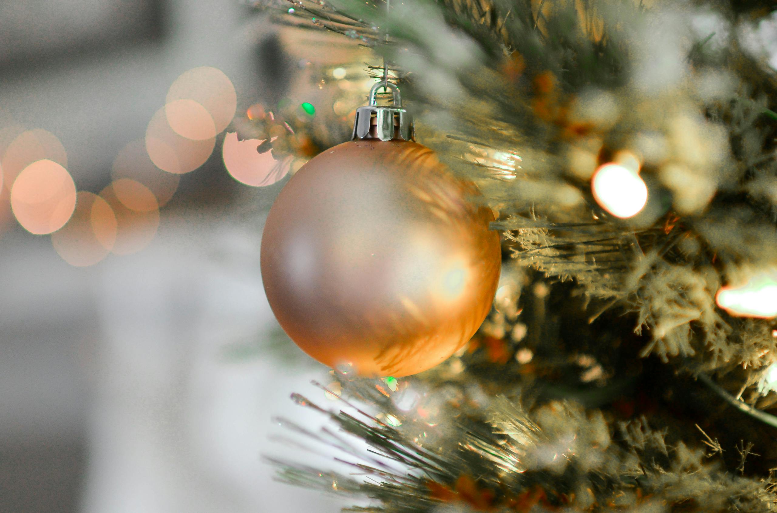 Close-up of a golden Christmas ornament hanging on a beautifully decorated tree with blurred festive lights.
