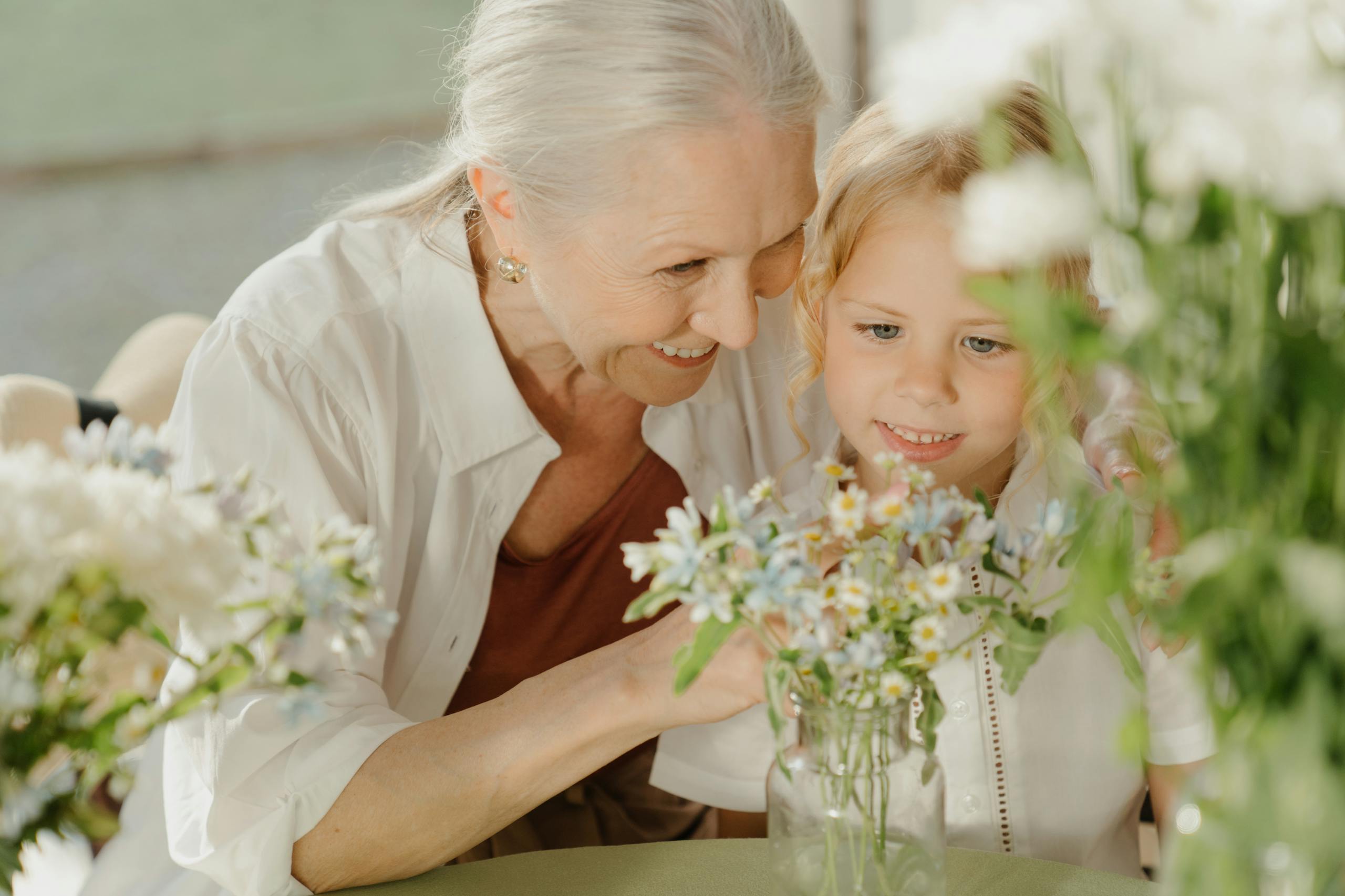 Grandmother and grandchild enjoying flowers at a table, sharing a joyful moment together indoors.